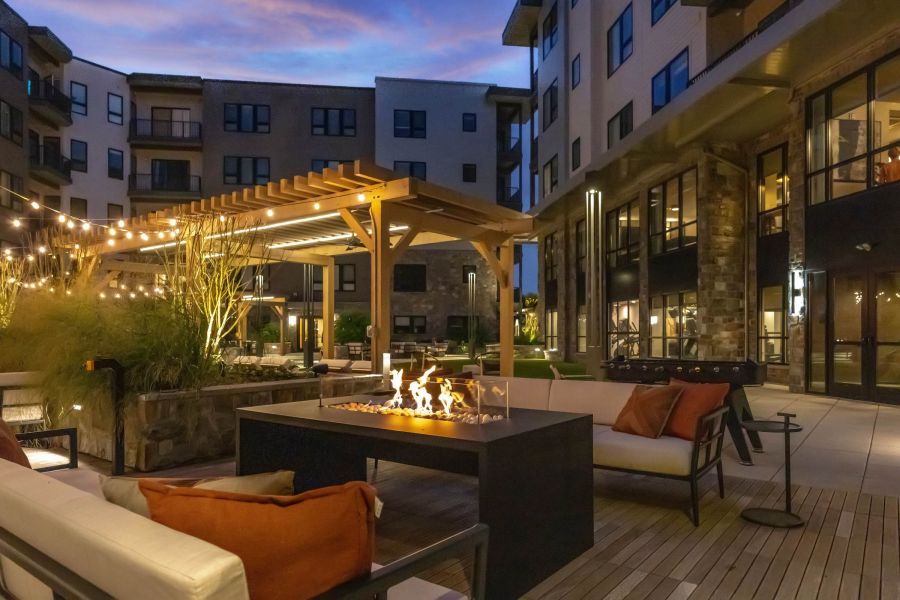 Modern apartment courtyard at dusk with a fire pit, string lights, and cozy outdoor seating.