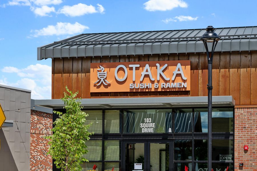 Front entrance of Otaka Sushi & Ramen restaurant with plants and a clear blue sky above.