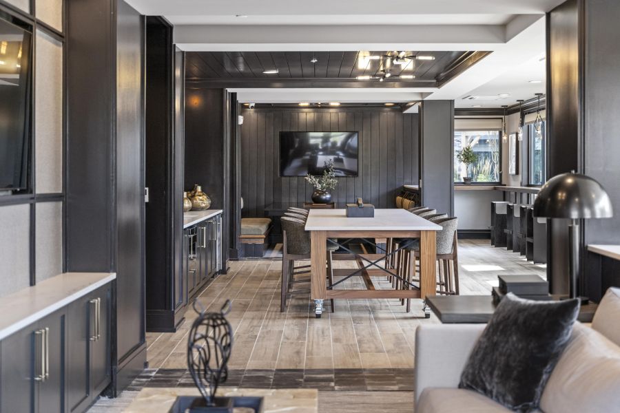 Modern lounge with wood floors, a large TV, bar seating, and neutral-toned furniture in an open-concept space.