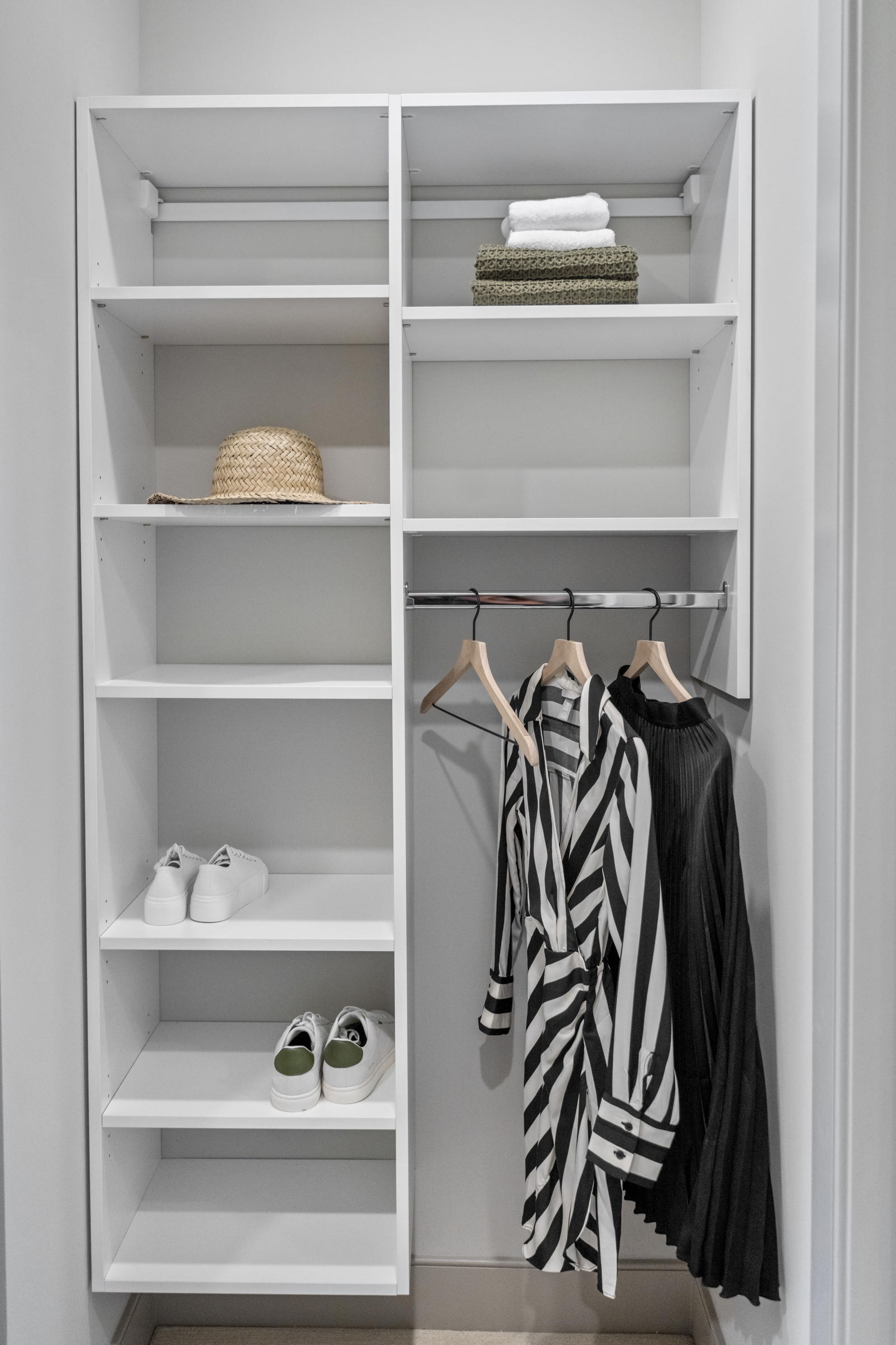 Minimalist closet with shelves, folded towels, a hat, two pairs of shoes, and three hanging garments.
