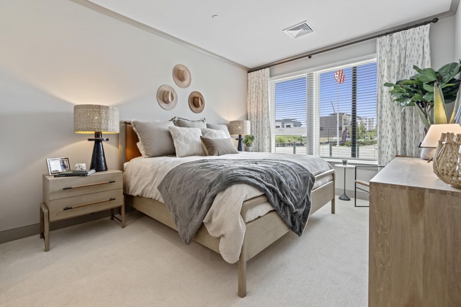Modern bedroom with a large bed, neutral decor, bedside lamps, and a window with city view.