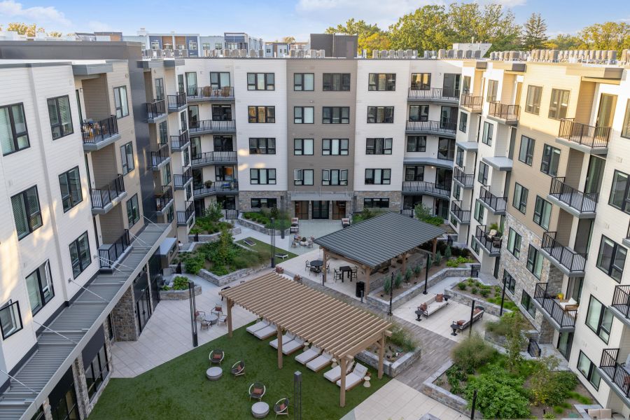A modern apartment complex courtyard featuring pergolas, seating areas, and landscaped greenery.