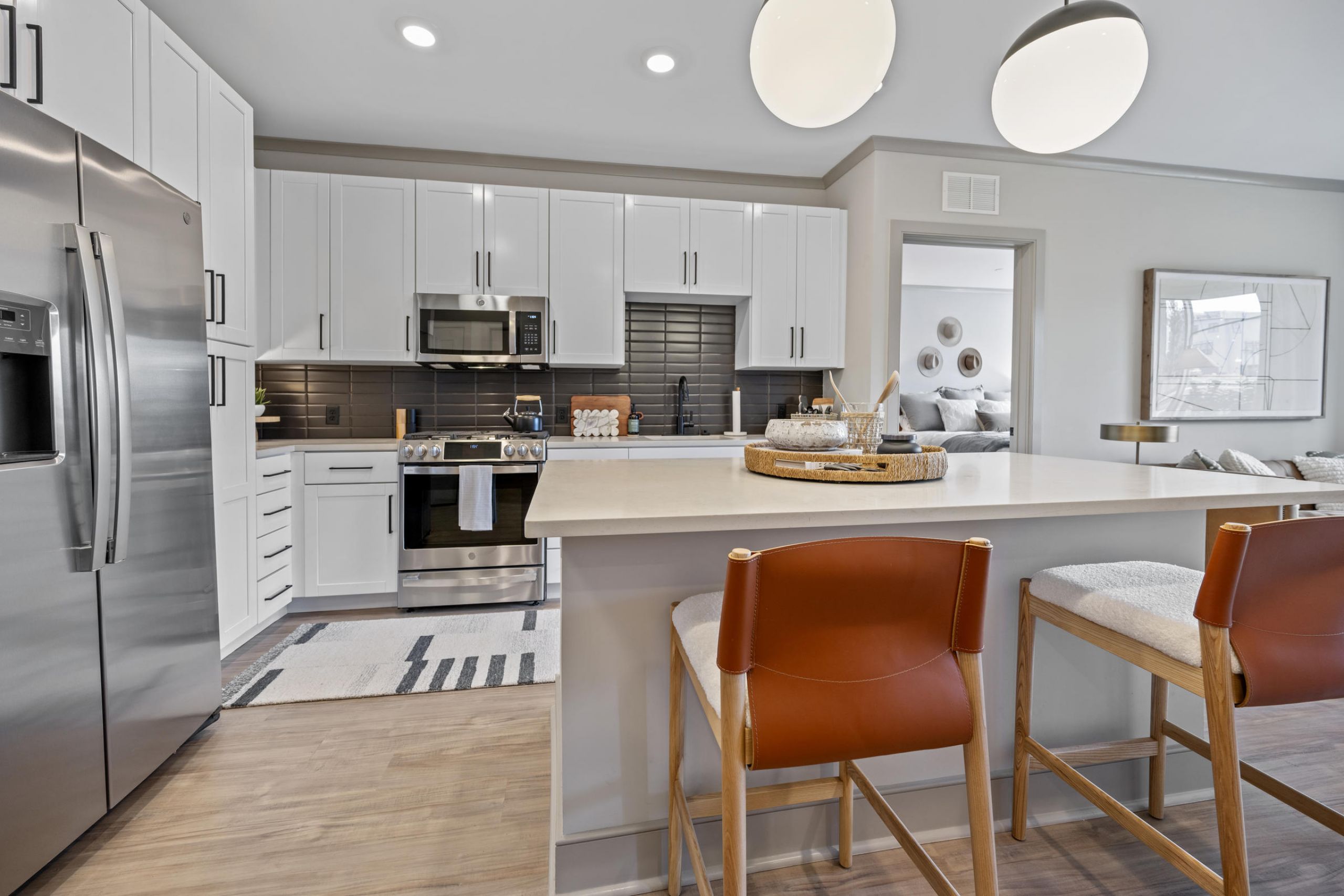 Modern kitchen with white cabinets, stainless steel appliances, and two brown chairs at a large island.