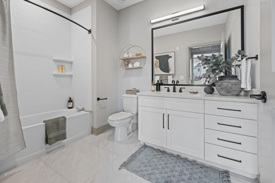 Modern bathroom with white cabinets, large mirror, bathtub, and decorative plants on the counter.