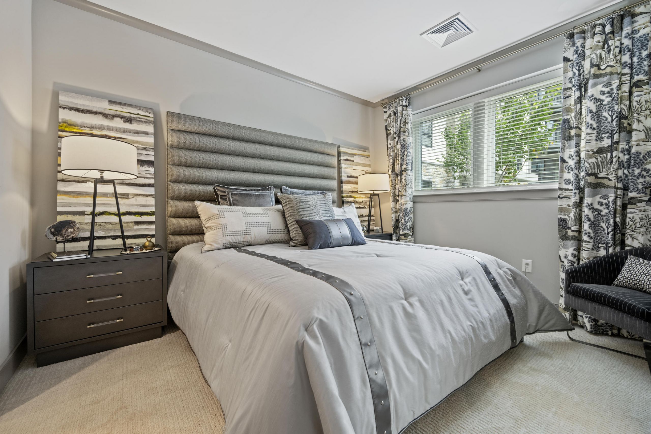 Modern bedroom with a large bed, two nightstands, lamps, and a window with patterned curtains.