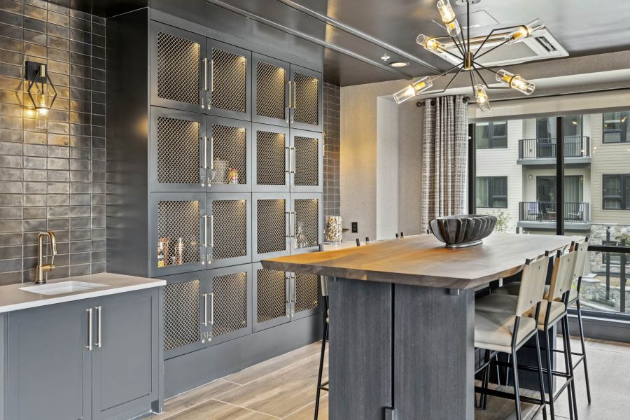 Modern kitchen with dark cabinets, mesh storage, a tall island, pendant lighting, and large windows.