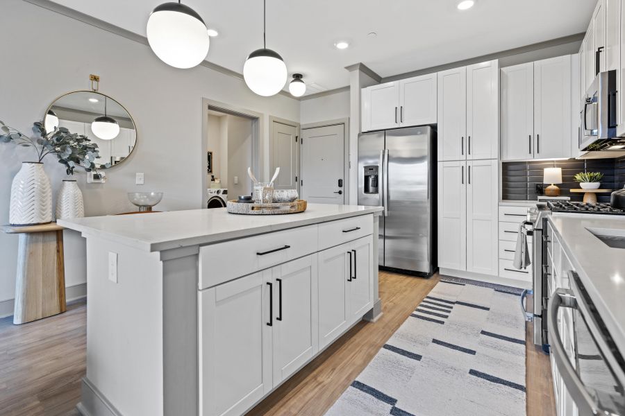 Modern kitchen with white cabinets, stainless steel appliances, island, and round pendant lights.
