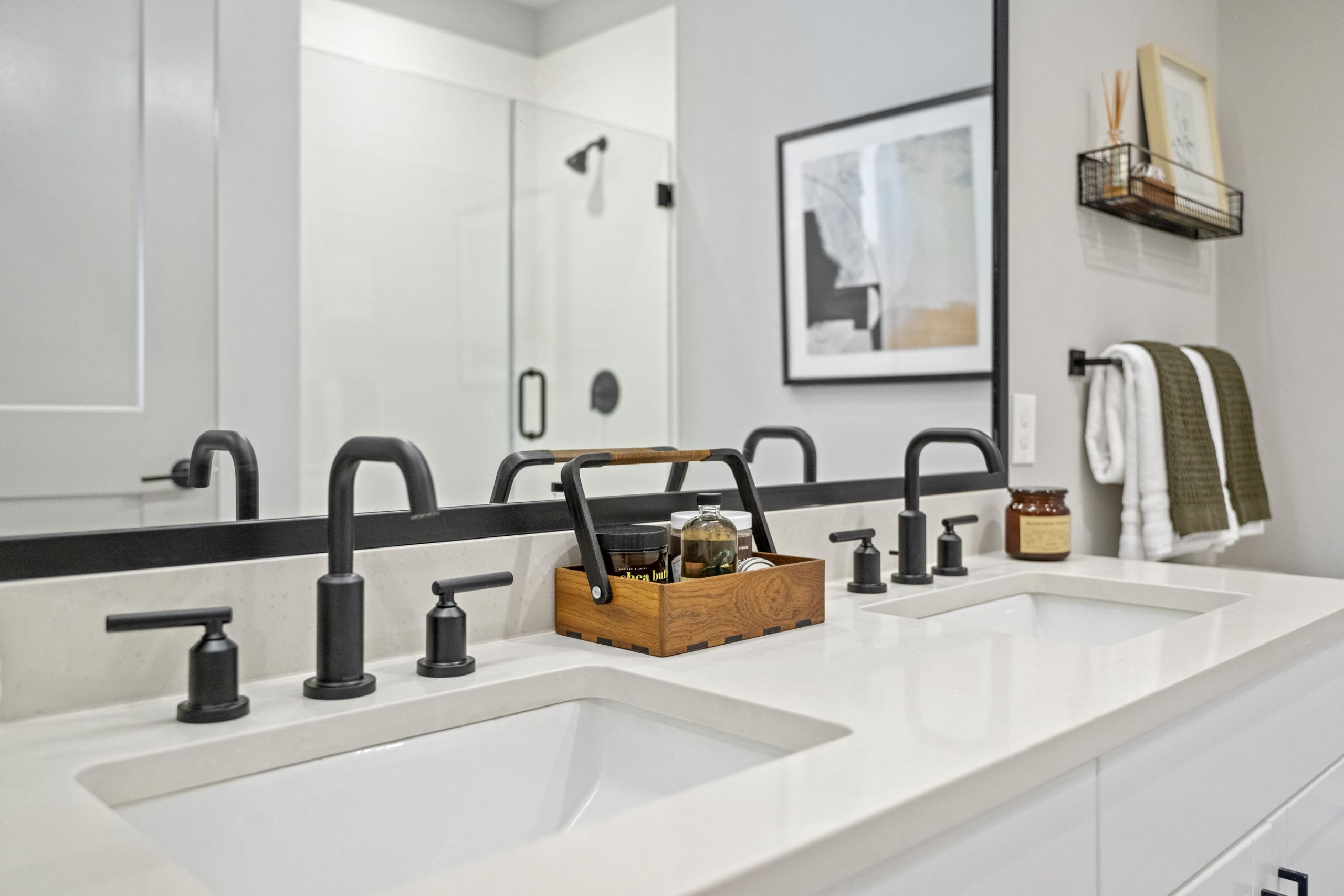 Modern bathroom with double sinks, black fixtures, and a wooden tray holding toiletries on the white countertop.