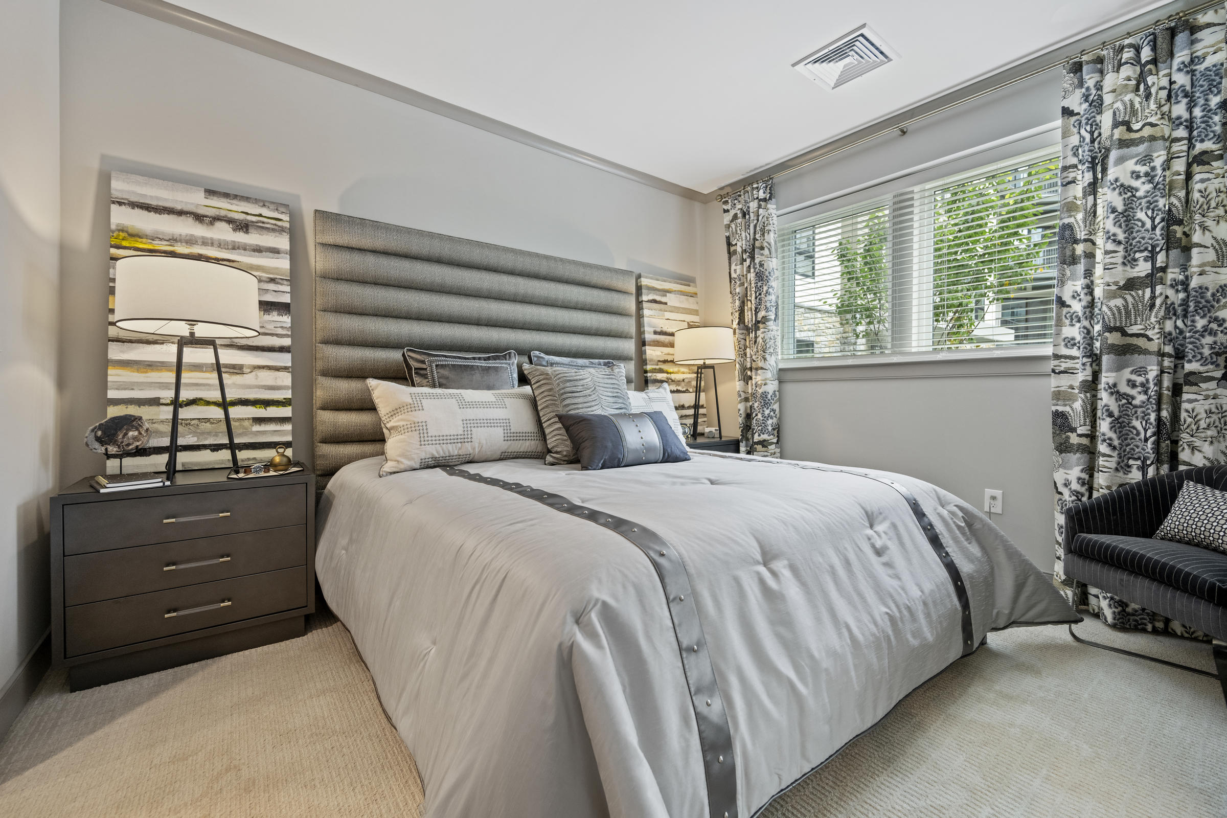 Modern bedroom with a large bed, two nightstands, lamps, and a window with patterned curtains.