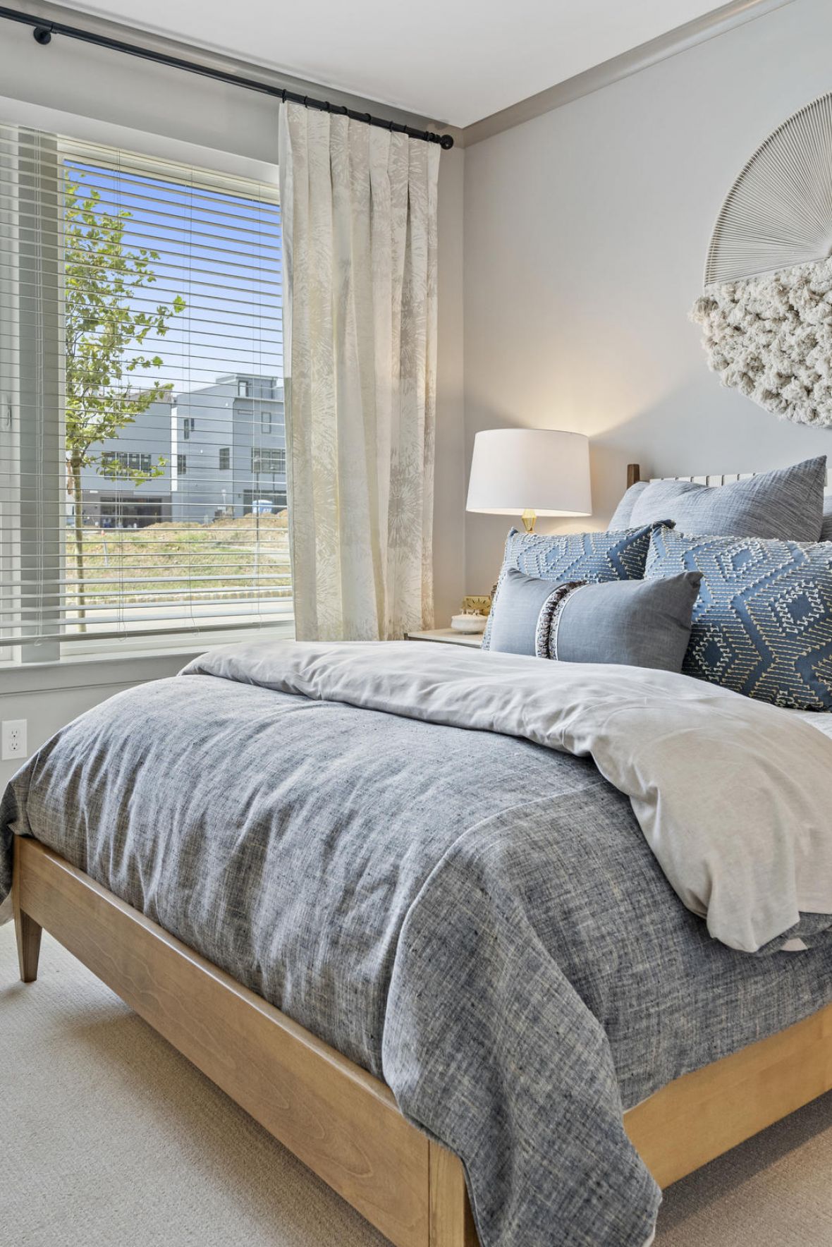 Bright bedroom with a made bed, blue and white bedding, large window, and modern decor on the wall.