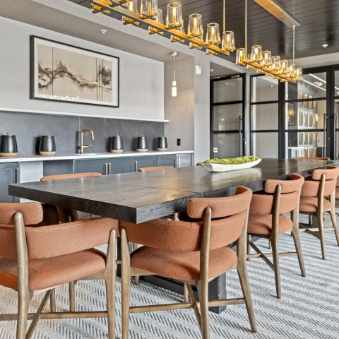 Modern dining room with a long wooden table, orange chairs, overhead lights, and a minimalist decor.