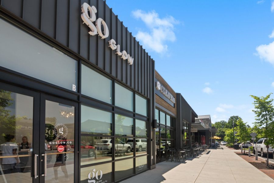 Modern storefronts with glass windows and outdoor seating on a sunny day with a clear blue sky.