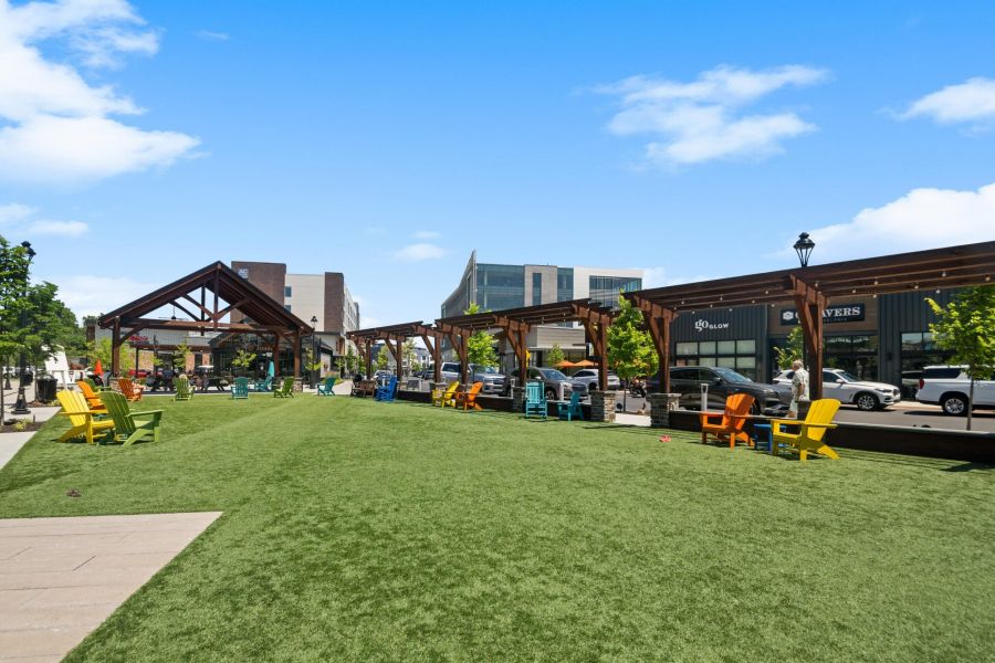 Outdoor park with green artificial grass, colorful chairs, and wooden pergolas in an urban setting.