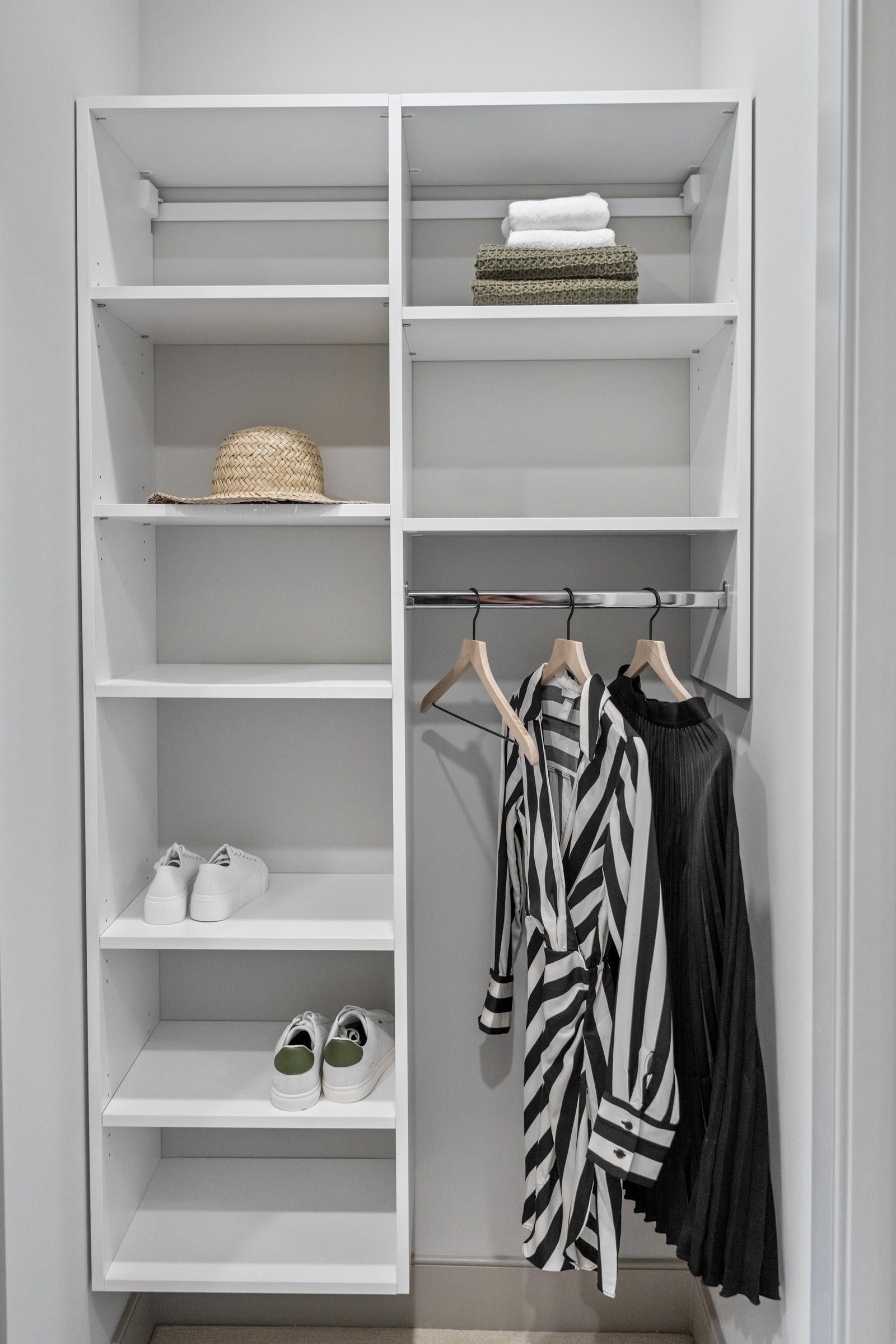 Minimalist closet with shelves, folded towels, a hat, two pairs of shoes, and three hanging garments.