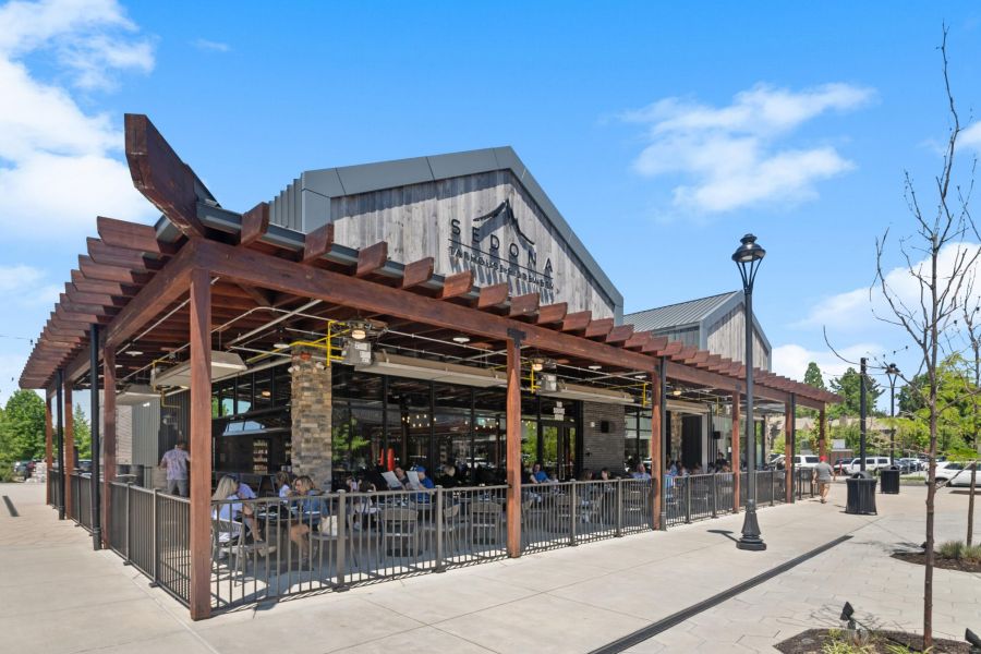 Outdoor seating area of a modern restaurant with people dining under a wooden pergola on a sunny day.