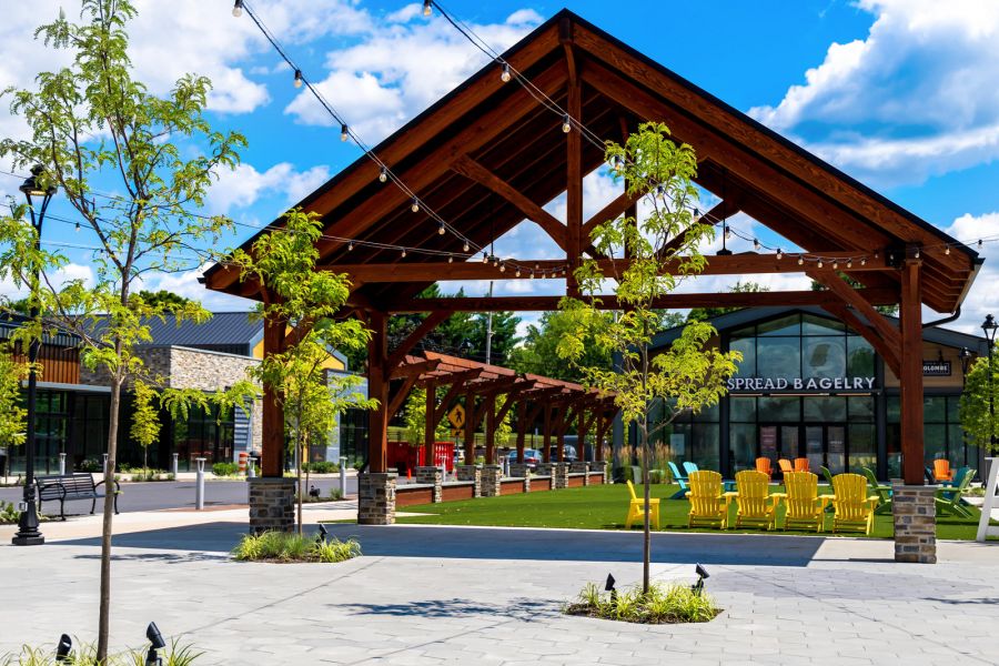Open-air pavilion with yellow chairs, string lights, and trees on a sunny day with a blue sky.