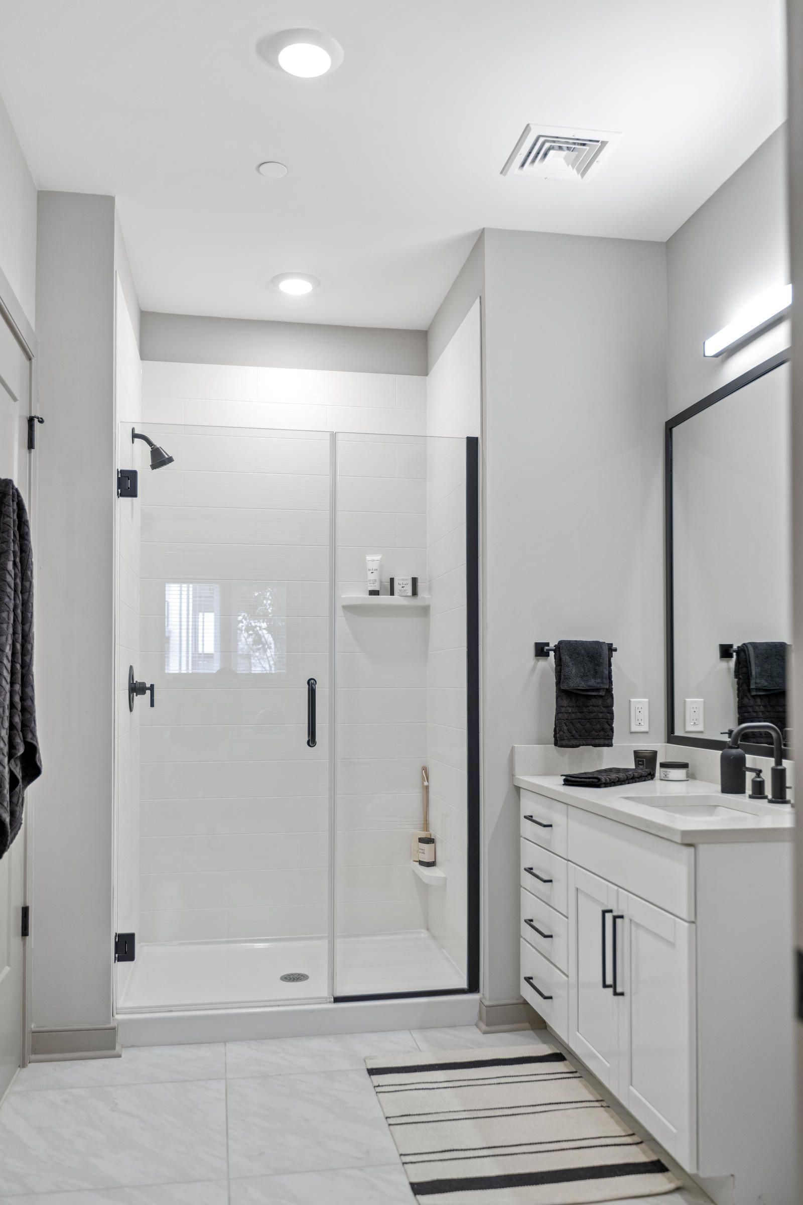 Modern bathroom with a glass shower, white cabinets, a striped rug, and black towel accents.