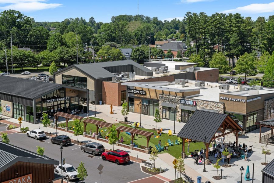 A modern shopping center with shops, outdoor seating, and people gathered on a sunny day.