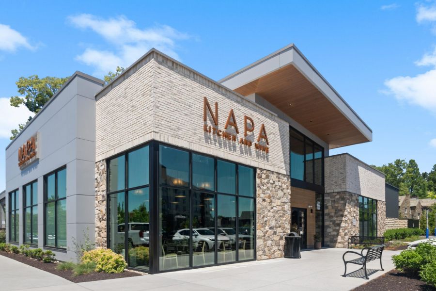 Modern restaurant with large windows and stone accents, featuring the sign "NAPA Kitchen + Bar" on the facade.
