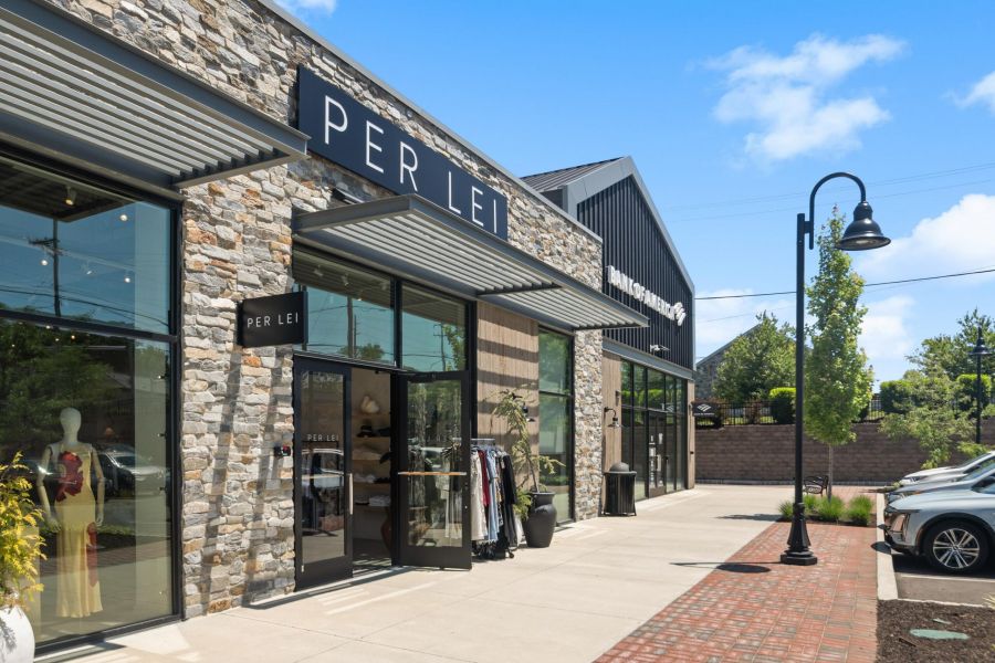 Exterior of a modern clothing store called PER LEI with glass windows and clothes displayed outside on a sunny day.