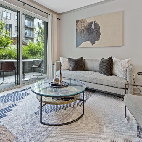 Modern living room with gray sofa, glass coffee table, and large sliding doors leading to a patio with chairs.