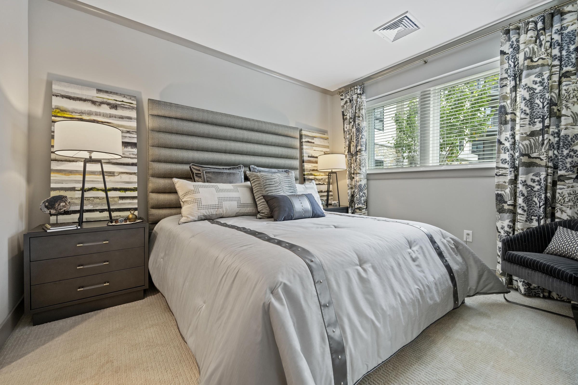 Modern bedroom with a large bed, two nightstands, lamps, and a window with patterned curtains.